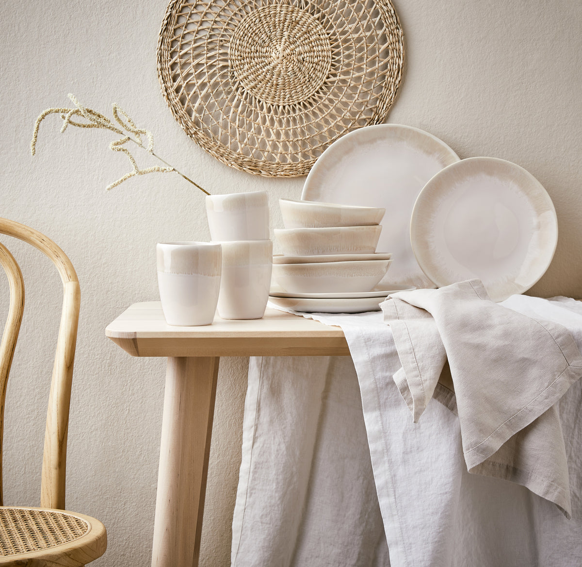 Beige-weißes Keramik Geschirr mit Glasur auf einem Holztisch mit beiger Tischdecke angerichtetet.