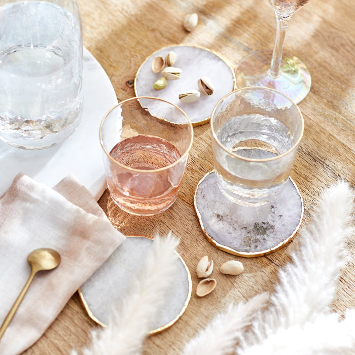 Elegante Untersetzer für Gläser mit Goldrand auf einem rustikalen Holztisch, kombiniert mit Wassergläsern und weiß-goldener Dekoration.