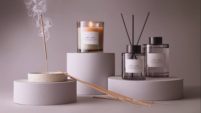 Ciel Libre Raumduft-Set aus Duftkerze im Glas, Diffuser mit schwarzen Stäbchen und Räucherstäbchen auf grauen runden Podesten im minimalistischen Stil.